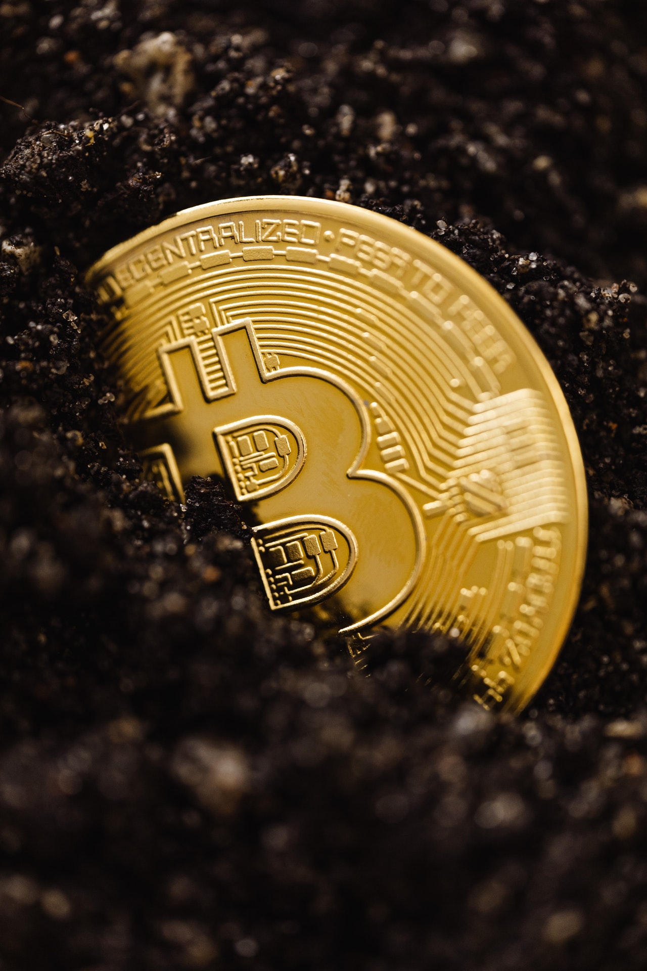 A bitcoin lying partially covered, in dirt